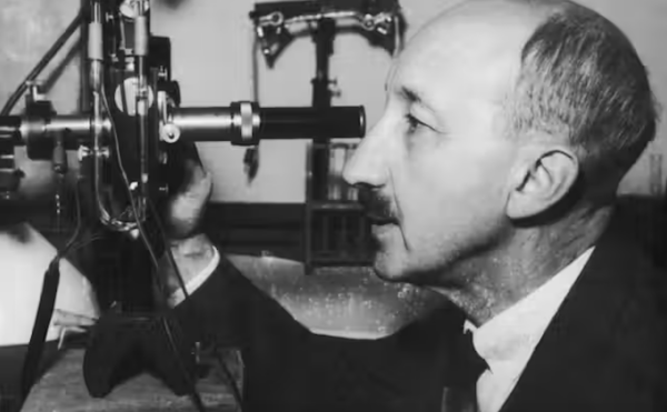 Black and white image of man looking into microscope